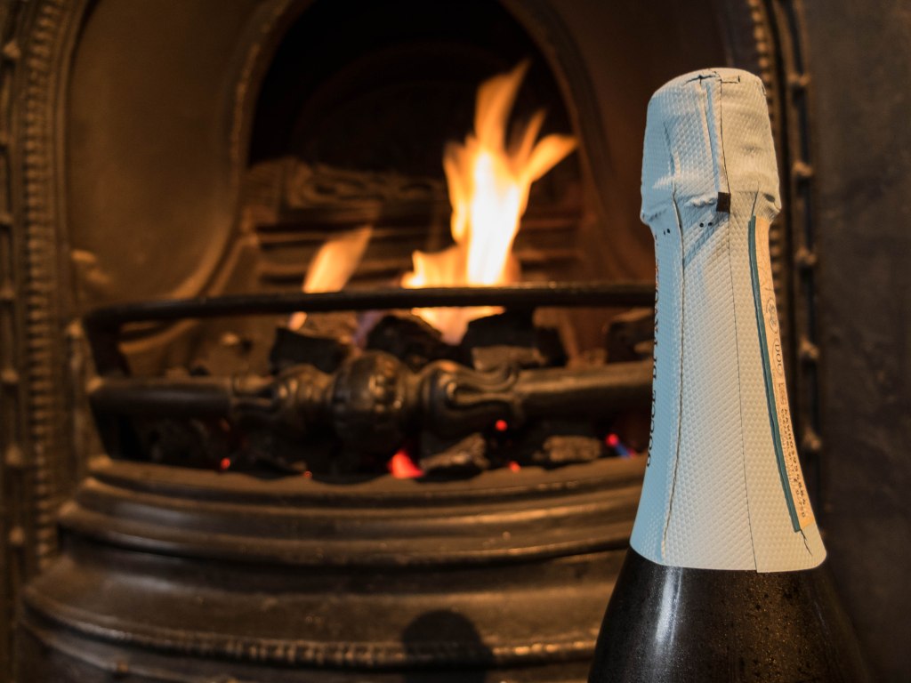 The neck of a bottle of prosecco in front of a fire.